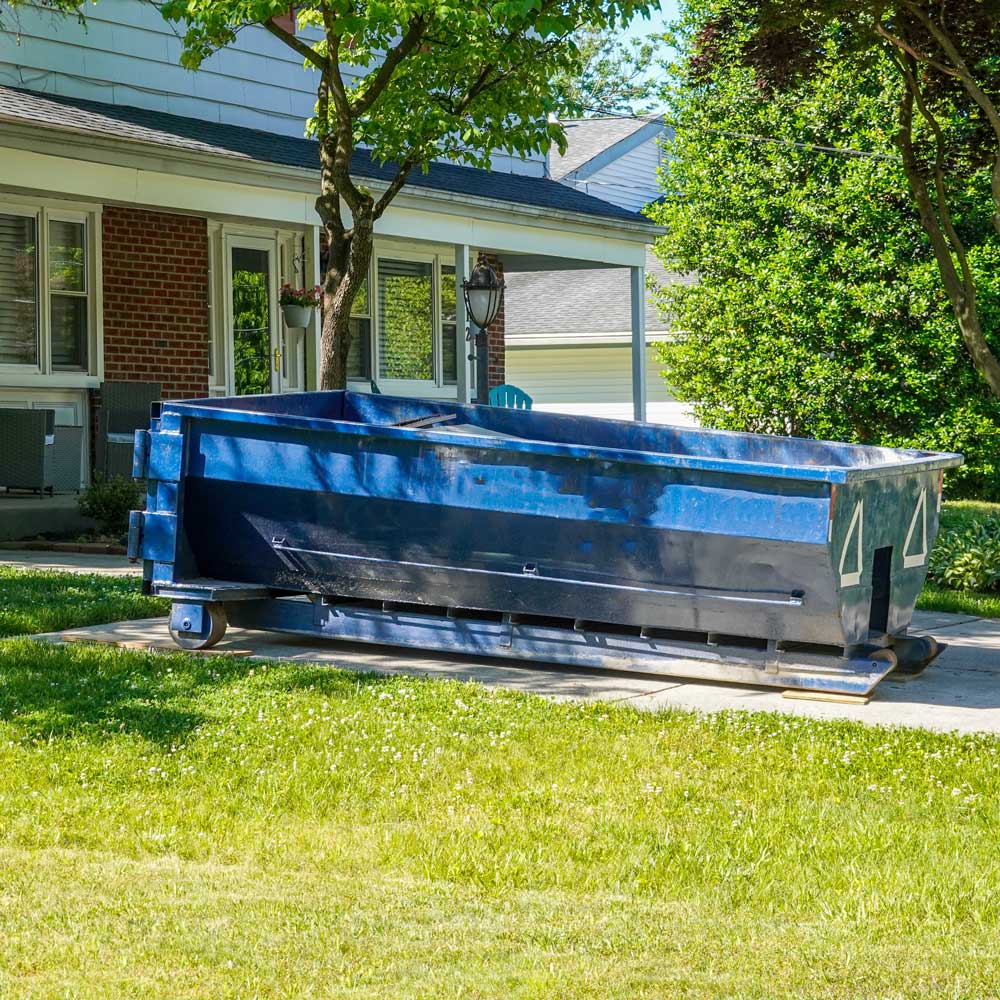 A large blue dumpster sits on a driveway. The dumpster is used for waste management.