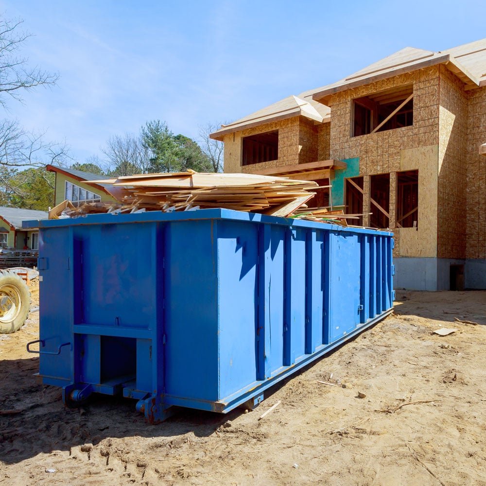 A large blue dumpster on a construction site. The dumpster is filled with wood and other building materials.