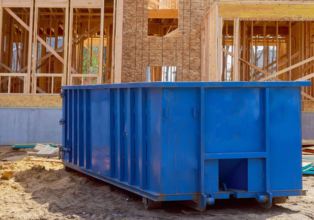 A large blue dumpster sits on a construction site. The dumpster is used for waste removal during building process.