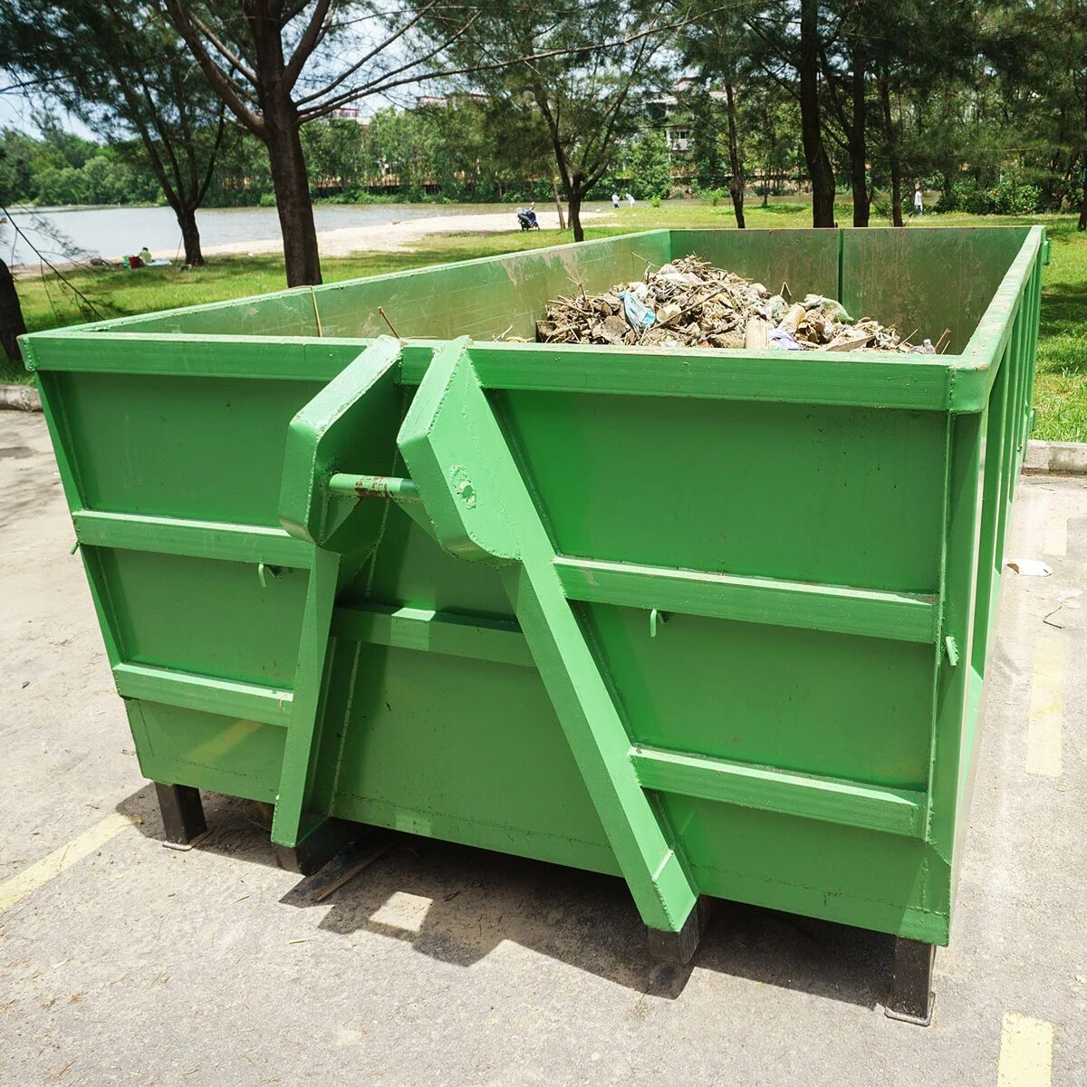 A green metal dumpster filled with construction waste. It is placed on a concrete surface.