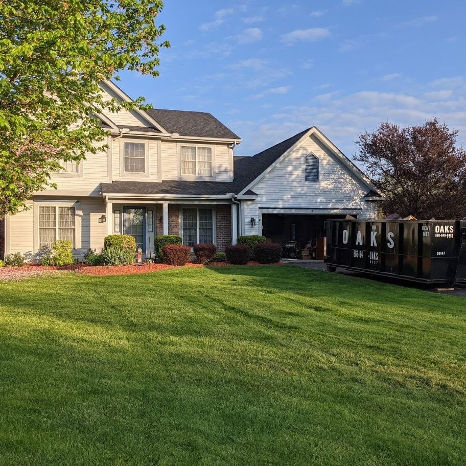 A large house with a green lawn and driveway. The house has a covered porch and a two-story structure.